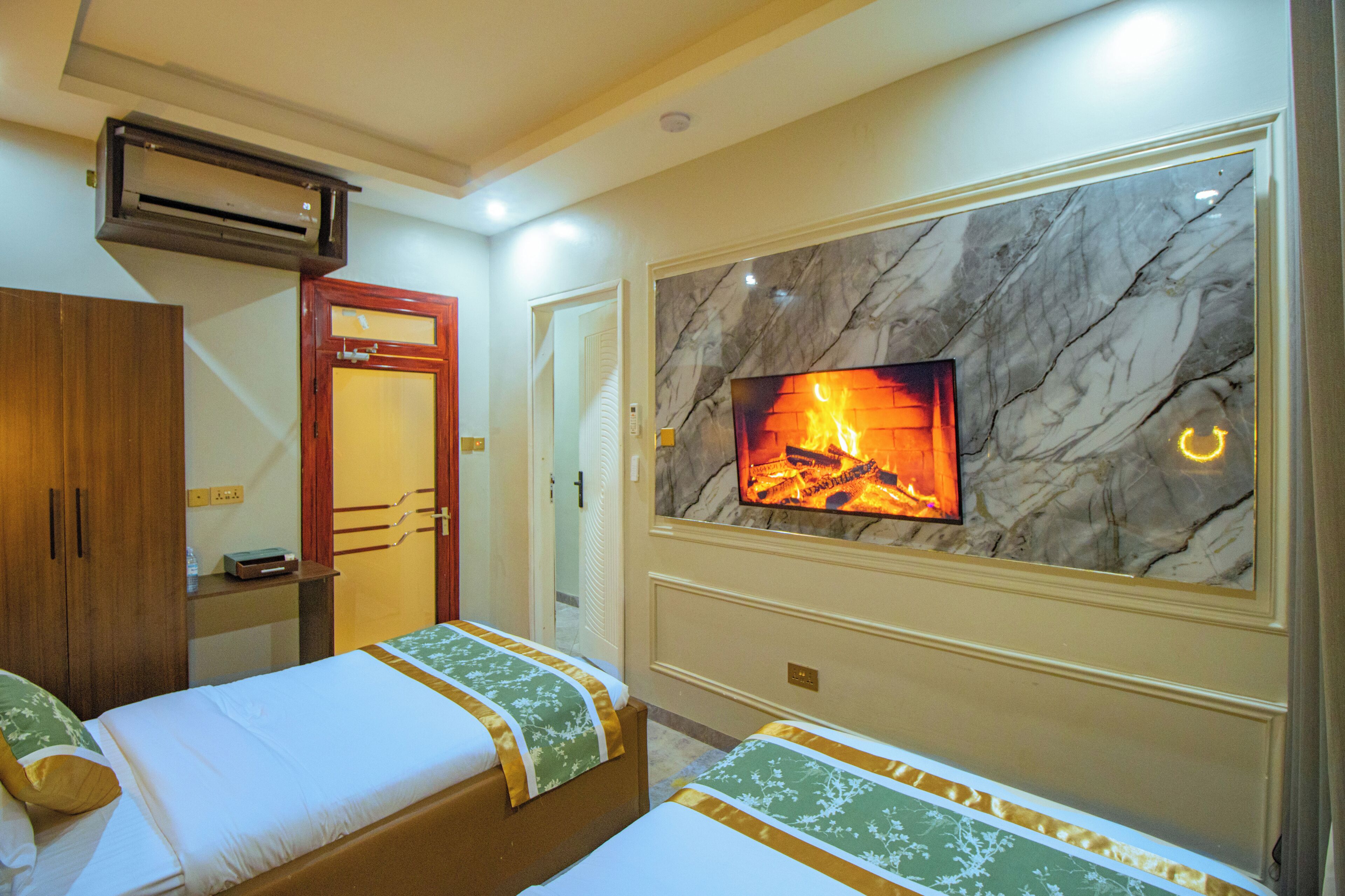 Habitación de hotel con dos camas, un televisor montado en una pared de mármol, un aire acondicionado y un armario de madera.