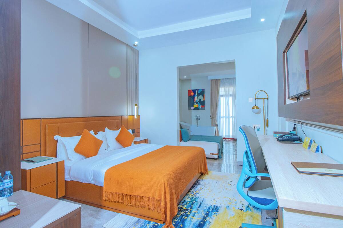 Habitación de hotel con cama, escritorio, silla y vista al pasillo.