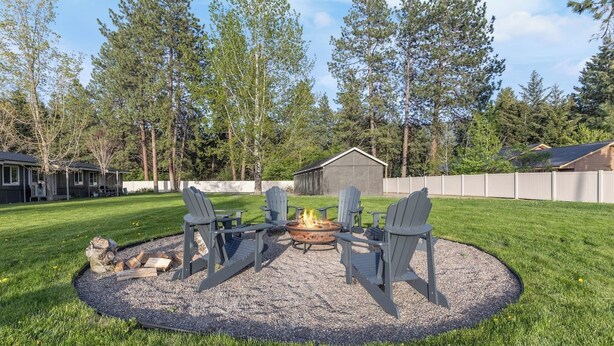 A backyard with a fire pit, four Adirondack chairs, and a gravel circle.