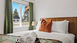 A hotel room with a bed, a window with curtains, a lamp, and a view of the outside.