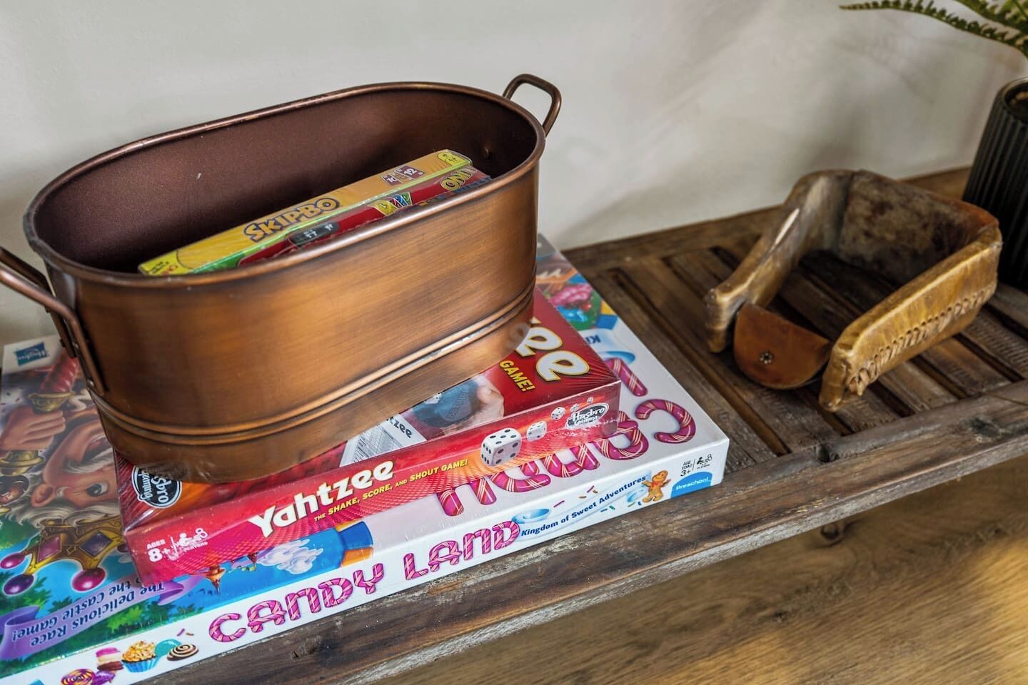 A copper pot on a wooden tray with a board game and a wooden brush.