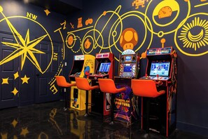Arcadespelautomaten met neonborden, een muurontwerp met een sterrenkompas en oranje stoelen.