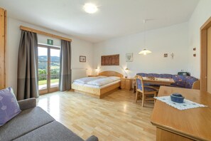 Ein Schlafzimmer mit einem Bett, einem Schreibtisch, einem Sessel, einer Couch und Blick ins Freie.