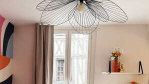 Ein modernes Wohnzimmer mit einer Couch, einem Couchtisch und einem Sessel. Ein Fenster mit Vorhängen, eine Heizung und Regale mit Dekorationselementen sind ebenfalls zu sehen.