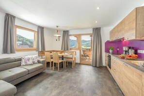 Une cuisine moderne avec des meubles en bois, un coin repas avec une table et des chaises, un canapé et de grandes fenêtres avec des rideaux.