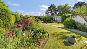 A garden with a pathway leading to a house, surrounded by various plants and a greenhouse. - Rêves d'Emeraude – Côte et Cœur Room (Cancale)