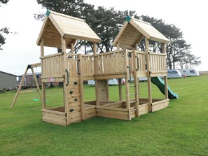 Eine Holzspielanlage mit Rutsche, Kletterwand und offenen Plattformen.