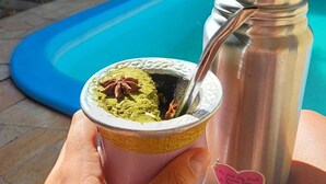 En person holder en kop matcha med en ske, ved siden af en rustfri vandflaske med et hjerteformet klistermærke.