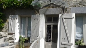 A stone building with a white door, shutters, and a small garden area with potted plants. - Rêves d'Emeraude – Le Rêve du Pêcheur Guest Room (Cancale)