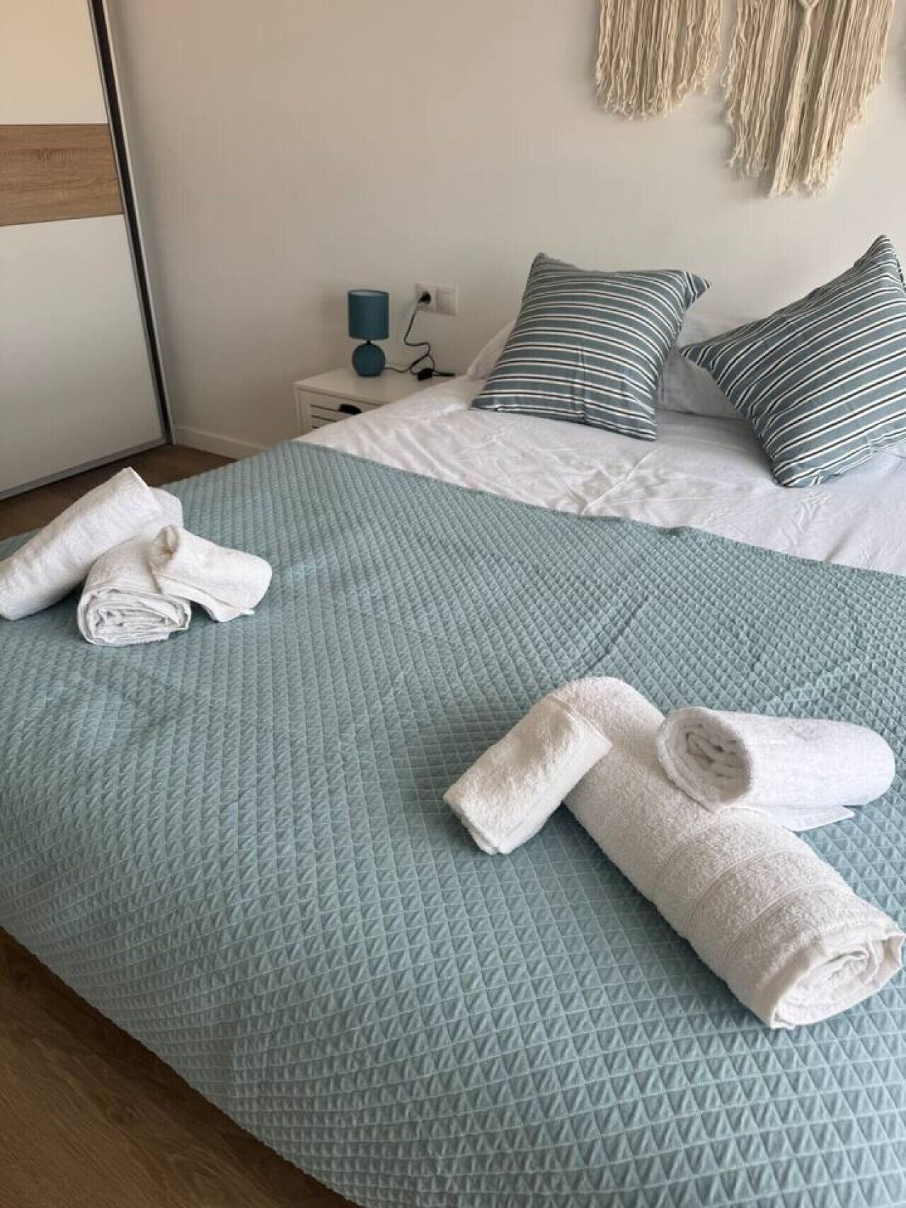 Ein Hotelzimmer mit einem Bett, einem Nachttisch, einer Lampe und einer Wanddekoration aus Makramee.