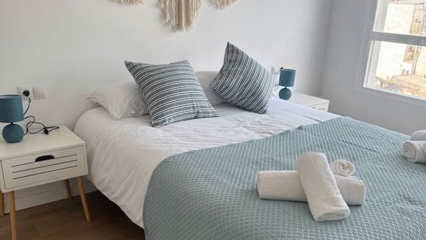 A neatly made bed with a blue quilt, two striped pillows, and a macrame wall hanging. - 4-Bedroom Beach Apartment in Ribeira | Ocean Views & Just Steps from the Beach (Ribeira)