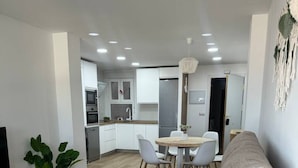 A modern living room with a sofa, dining table, and kitchen in the background. - 4-Bedroom Beach Apartment in Ribeira | Ocean Views & Just Steps from the Beach (Ribeira)