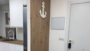 A modern kitchen with white cabinets, a wooden accent wall, a stainless steel refrigerator, and a door with a handle. - 4-Bedroom Beach Apartment in Ribeira | Ocean Views & Just Steps from the Beach (Ribeira)