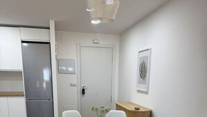 A modern kitchen with white cabinets, a stainless steel refrigerator, and a wooden dining table with white chairs. - 4-Bedroom Beach Apartment in Ribeira | Ocean Views & Just Steps from the Beach (Ribeira)