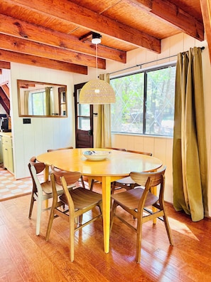 Una mesa de madera con sillas, una lámpara colgante y un ventanal con cortinas.