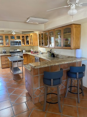 Eine Küche mit Granit-Arbeitsplatten, Edelstahlgeräten, Holzschränken und einer Bar mit Sitzgelegenheiten.
