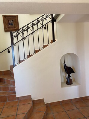 Eine Treppe mit dekorativer Metallreling, ein Holzbildrahmen an der Wand und eine Vogel-Skulptur auf einem Sockel.