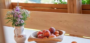 Ein Holztisch mit einer weißen Krug mit Blumen und einer Holztasse voll Obst.