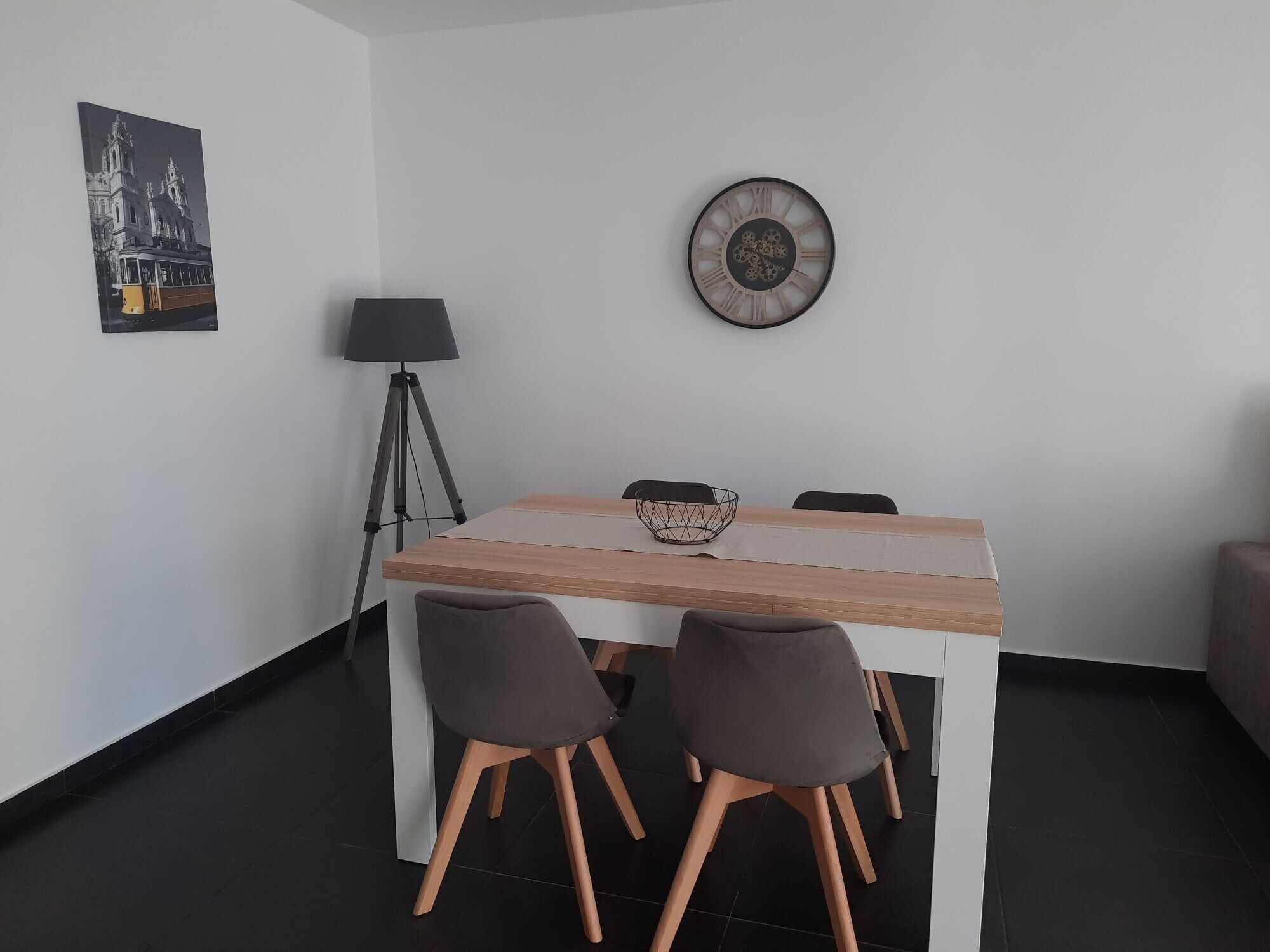 Un coin repas comprenant une table, des chaises, une lampe, une horloge et un tableau encadré accroché au mur.
