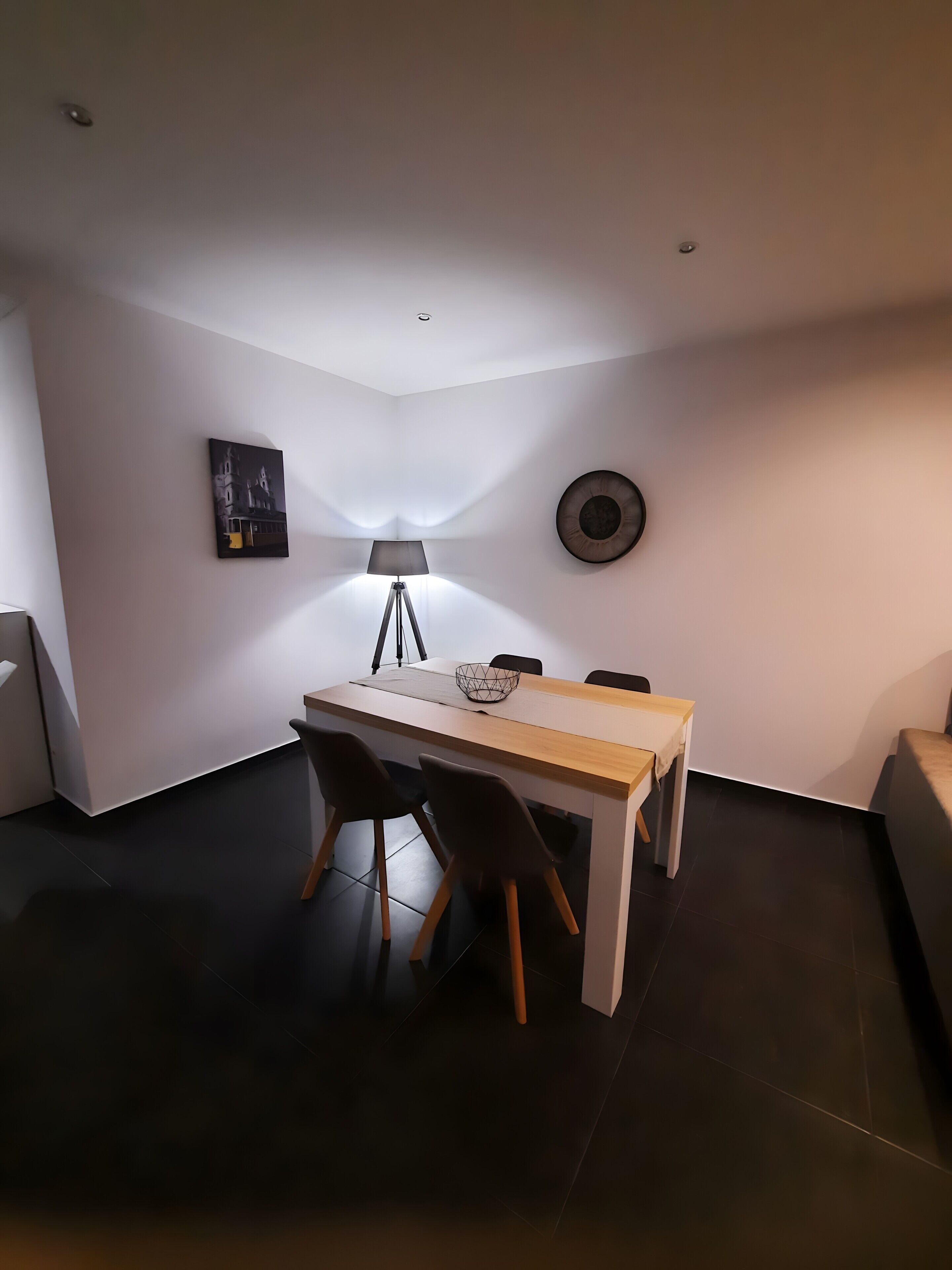 A dining area with a table and chairs, a lamp, a wall-mounted picture, and a round object.