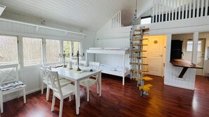 Una habitación con una cama litera, una mesa de comedor con sillas, una escalera y una ventana con vistas a un bosque.