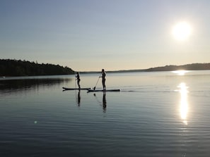 Two people paddleboarding on a calm lake with a forested shoreline and the sun low on the horizon. - 4 Star Holiday Home in Trollhattan (Trollhattan)