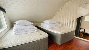 Dos camas con colchones y almohadas, piso de madera y una ventana.