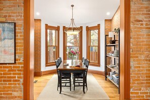 A dining area with a wooden table, chairs, a chandelier, and brick walls. - Historic Family-Friendly Gem Steps from Downtown, CU & Hiking Trails (Boulder)