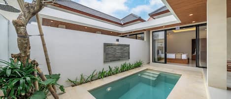 A modern house with a swimming pool, a tree, and a view of the sky.