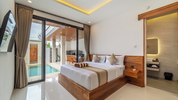 Un dormitorio moderno con una cama grande, cabecera de madera, mesita de noche integrada y baño con tocador de madera.