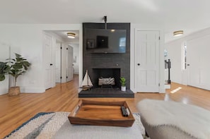 Ein modernes Wohnzimmer mit Kamin, Couchtisch aus Holz und einem darüber montierten Fernseher.