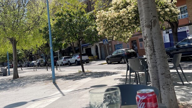 Una taula amb una llauna de Coca-Cola i un got de refresc, un arbre i cotxes aparcats al carrer.
