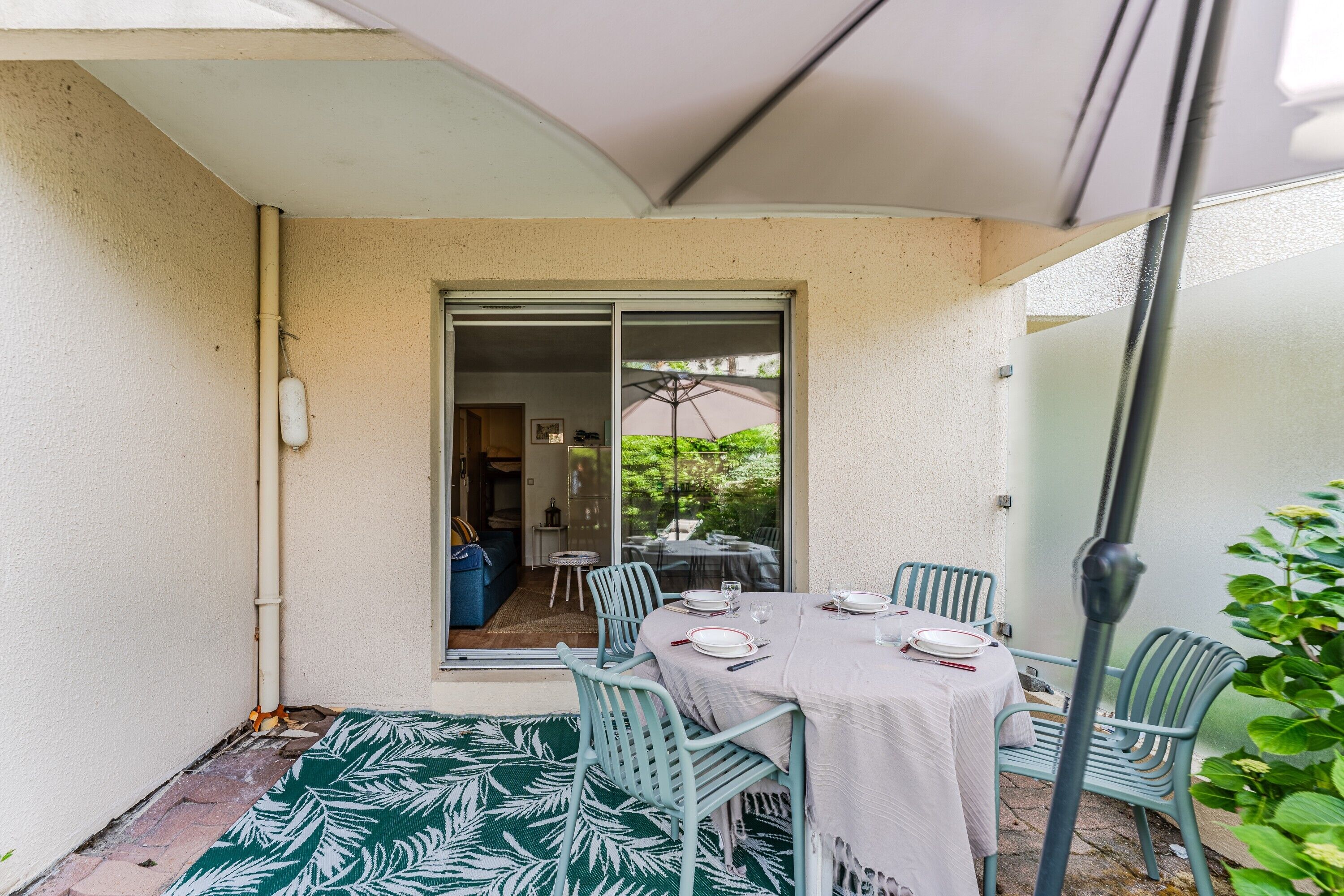 Eine Terrasse mit Tisch für vier Personen, umgeben von Stühlen, und eine Glastür, die zu einem Innenbereich führt.