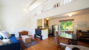 A spacious living area with a blue sofa, wooden dining table, and a kitchen in the background. - Hideaway in Quiet Bolinas Near the Beach (Bolinas)