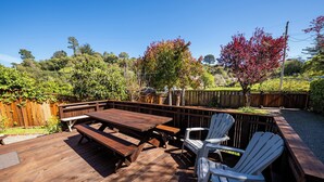 A wooden deck with picnic tables and white chairs, surrounded by a wooden fence and trees. - Hideaway in Quiet Bolinas Near the Beach (Bolinas)