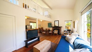 A spacious living room with a large TV, comfortable seating, a fireplace, and a balcony with a view. - Hideaway in Quiet Bolinas Near the Beach (Bolinas)