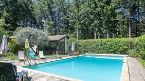 A rectangular swimming pool with a tiled edge, surrounded by lounge chairs and umbrellas, set in a landscaped garden with trees and a building in the background. - Holiday Home with Park, Private Pool, Wi-Fi, and Air Conditioning in Jaujac (Jaujac)