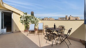 Eine Dachterrasse mit Tisch, Stühlen, einem Blumentopf und Blick auf die Stadt.