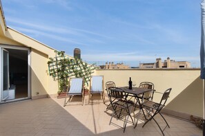 Una terraza en la azotea con una mesa y sillas, una planta en maceta y vistas del paisaje urbano.