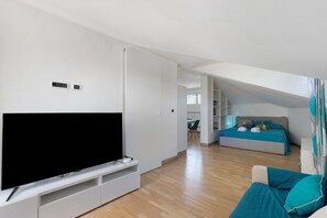 A modern living room with a flat-screen TV, a sofa, and a bed in the background. - Penthouse Between Sky and Sea with Panoramic Terrace - Lido Di Ostia (Lido di Ostia)