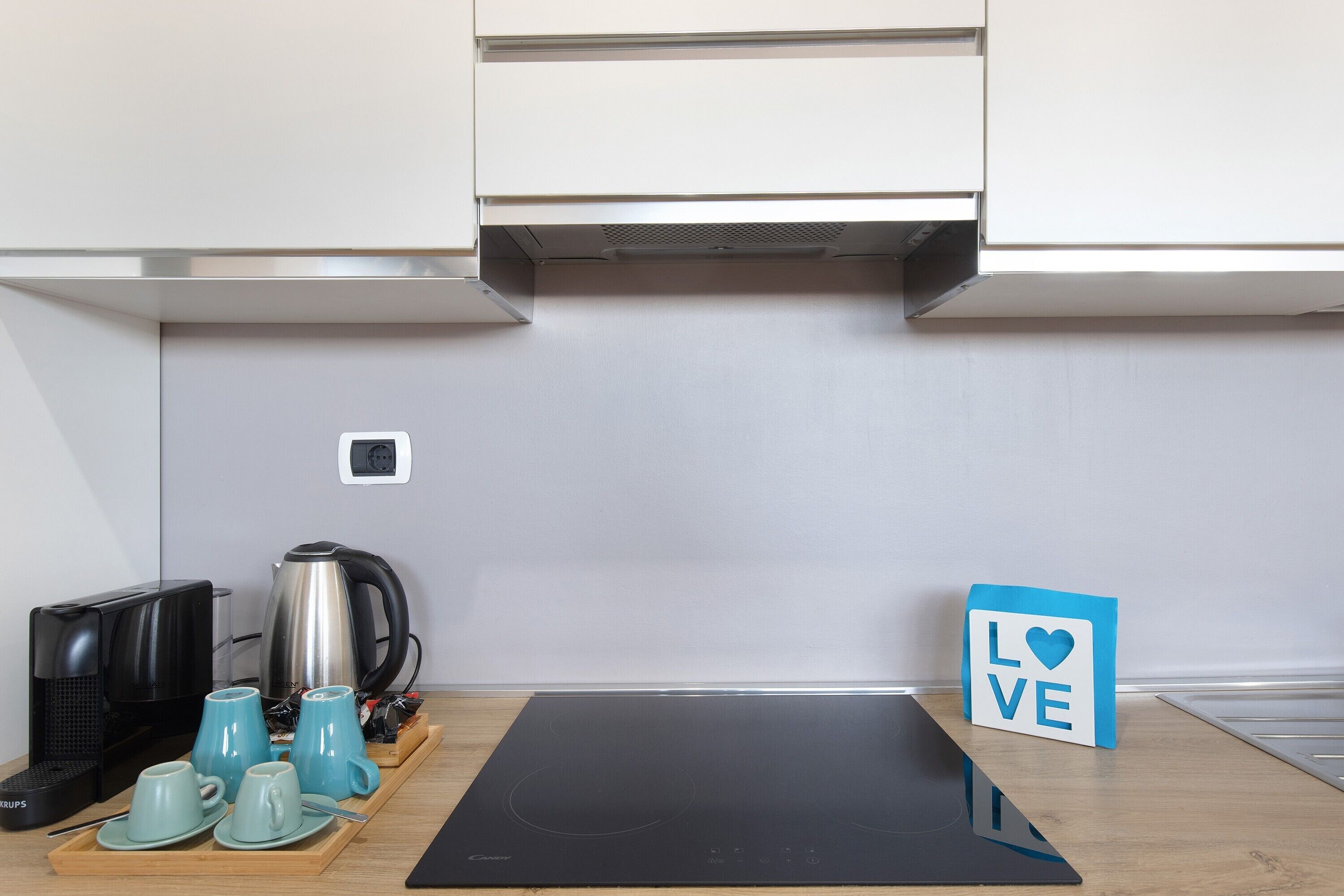 A kitchen with a black induction cooktop, a coffee maker, a kettle, and a 'LOVE' sign.