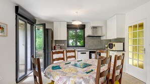 Spiseområde med et bord dækket til fire, et køkken med moderne hårde hvidevarer, og en skydedør til en balkon.