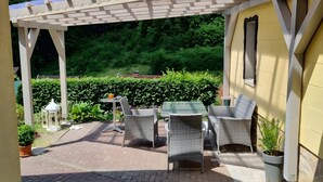 Ein überdachter Patio-Bereich mit Korbmöbeln, einem kleinen Tisch und einer Laterne.