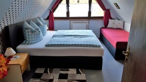 Ein Schlafzimmer mit einem Bett, einem Nachttisch, einer Lampe, einem Fenster mit Vorhängen und einer Heizung.