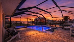 A pool area with a view of the sunset, lounge chairs, and a covered patio. - Saltwater Pool & Spa Villa on a Gulf-Access Canal (Englewood)