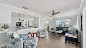 A modern living room with a sofa, armchairs, a coffee table, and a dining area with a kitchen in the background. - Saltwater Pool & Spa Villa on a Gulf-Access Canal (Englewood)