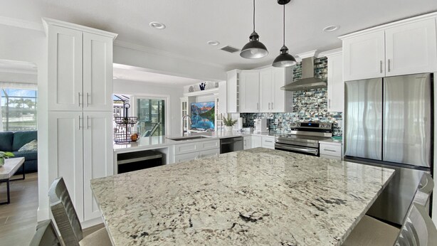 A modern kitchen with white cabinets, a granite island, stainless steel appliances, and pendant lighting. - Saltwater Pool & Spa Villa on a Gulf-Access Canal (Englewood)
