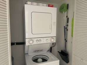 A compact laundry room with a front-loading washer and dryer, a mop, and a broom. - 2-bedroom condo in beautiful Punta Gorda with cool AC (Punta Gorda)