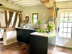 Cocina con isla central, vigas de madera, ventana con marco verde y puerta con paneles de vidrio.