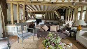 Ein rustikales Interieur mit freiliegenden Holzbalken, einer Steinwand, einem Essbereich und einer Couch mit Kissen.